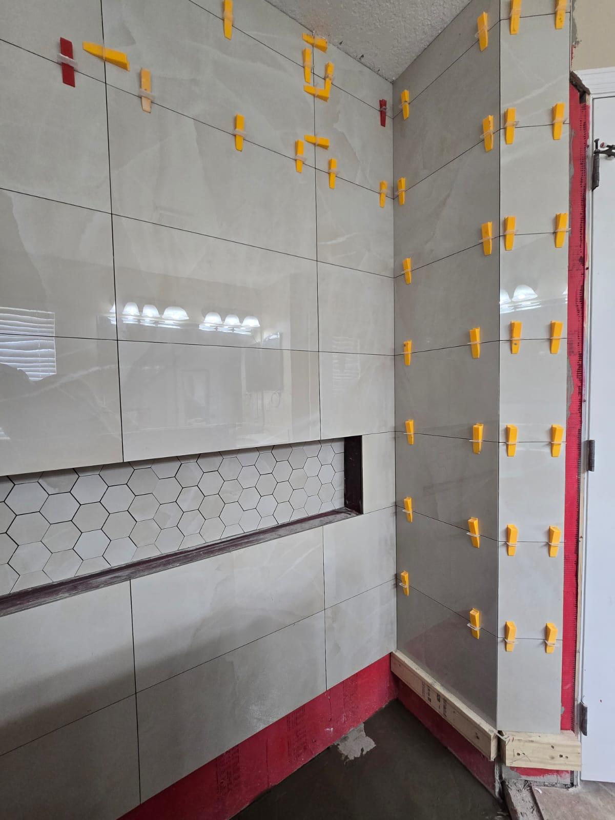 Large-format bathroom wall tile installation with leveling spacers and recessed niche