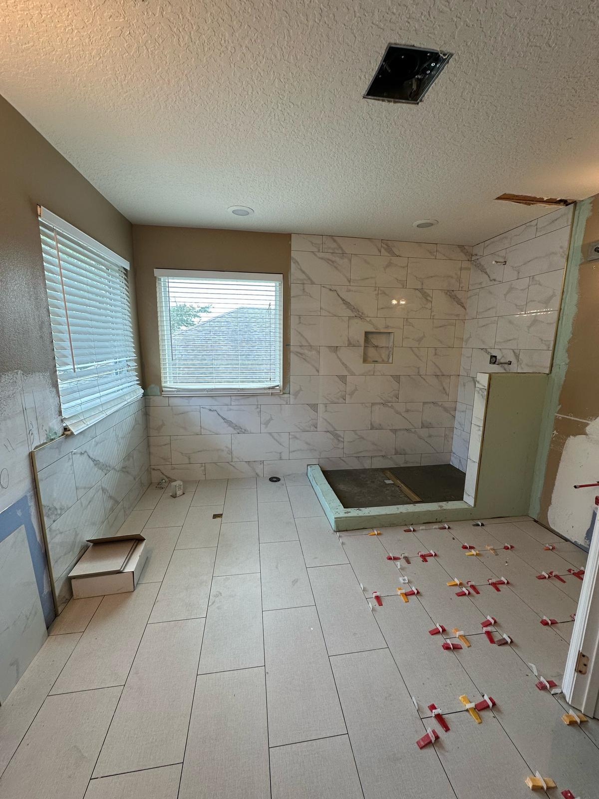 Bathroom renovation in progress with tiled floor and marble-look shower walls