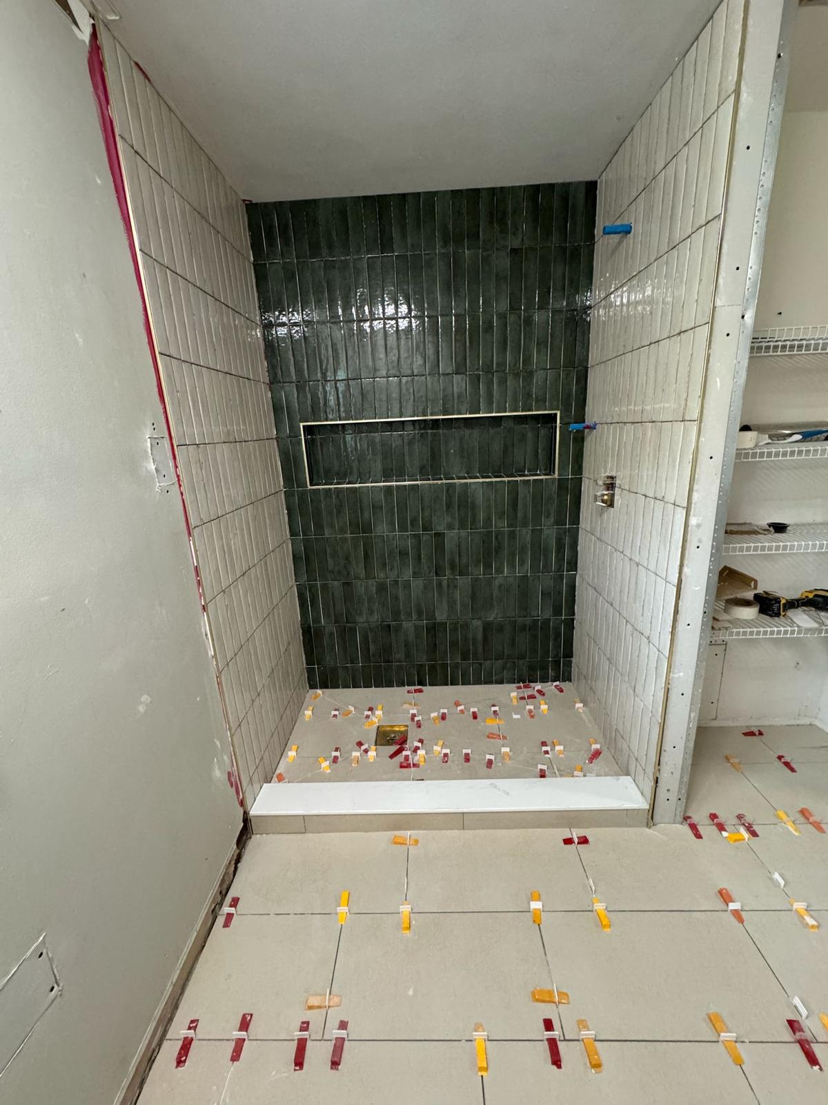 Walk-in shower installation with dark green feature tile and precision leveling spacers