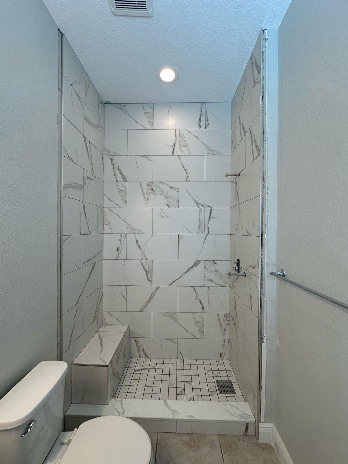 Compact walk-in shower renovation with marble-look tile and built-in bench