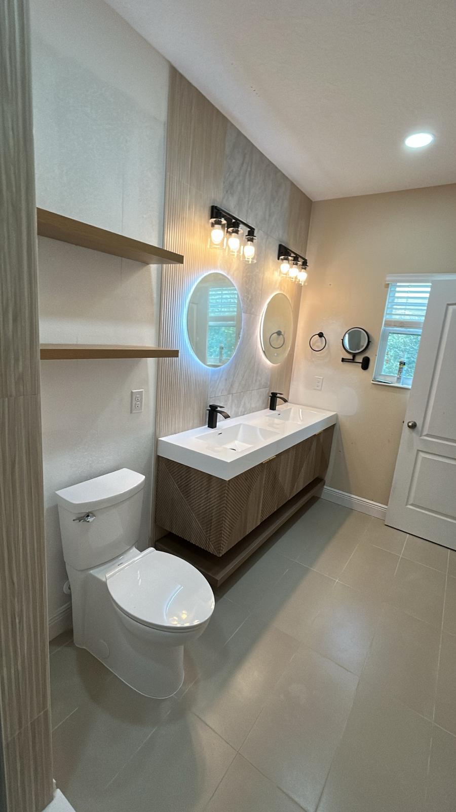 Completed bathroom with floating vanity, backlit mirrors and open wood shelving