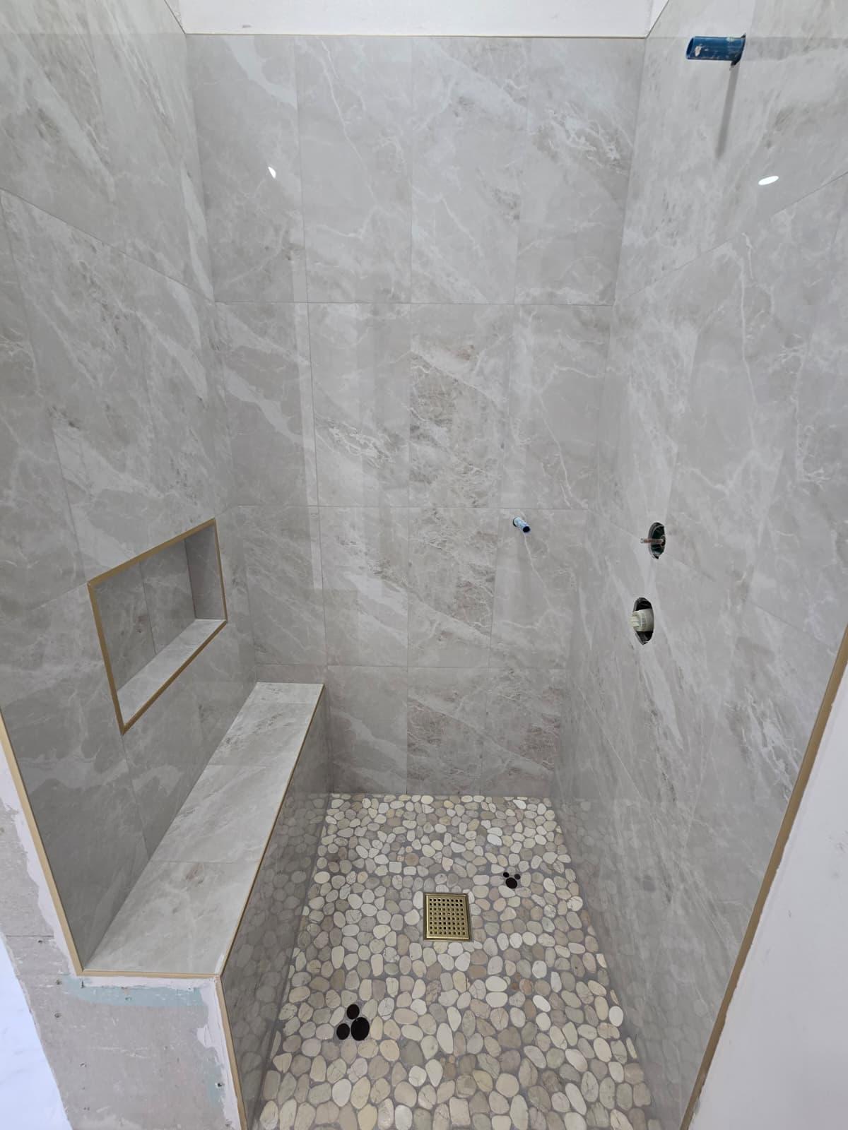 Shower installation with large-format marble walls, pebble floor and gold-trimmed niche