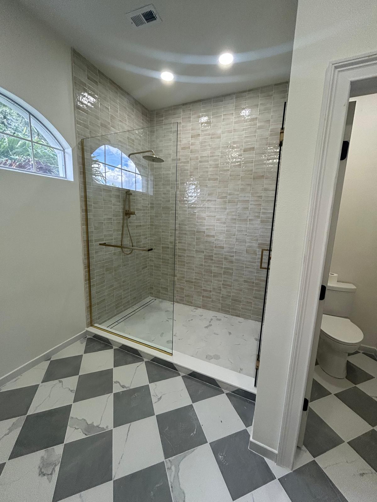 Glass-enclosed shower with gray mosaic tile and checkered marble-look floor