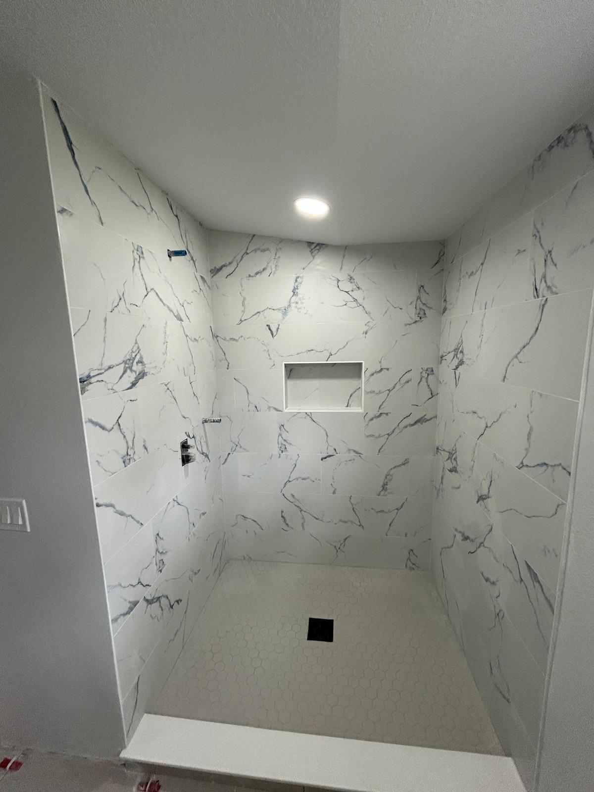Shower under construction with white marble-look tile and recessed niche