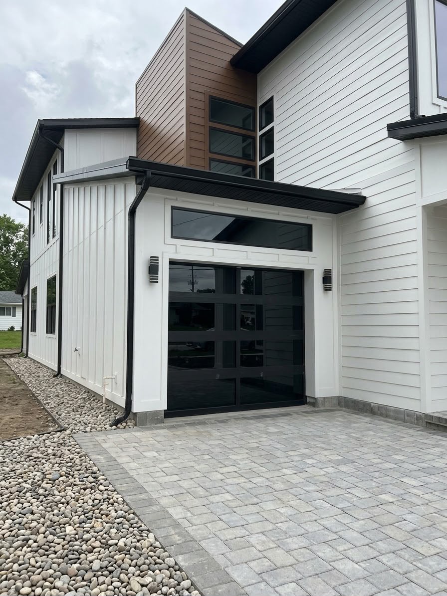 Modern home exterior with black garage door and stone-paver driveway