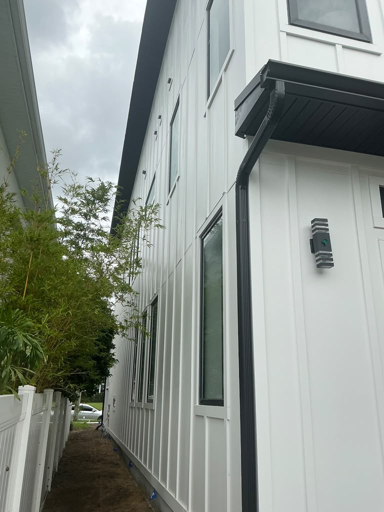 White board-and-batten siding with black gutter system alongside a bamboo garden path