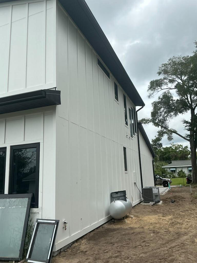 Side elevation of a white panel home with new gutters and exterior equipment pad