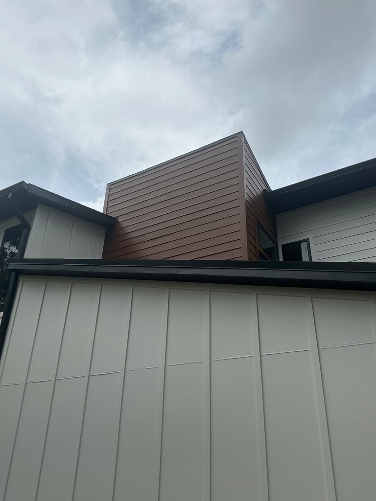 Modern wood-toned cladding volume above white paneled siding and black gutters