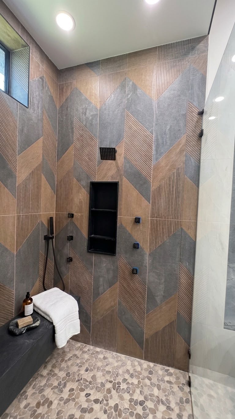 Walk-in shower with chevron tile walls, black fixtures, recessed niche and pebble floor