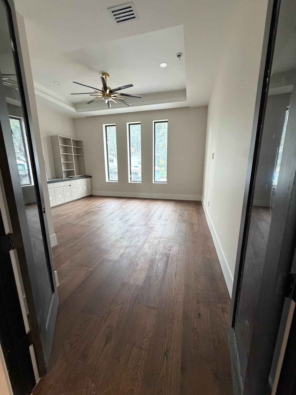 Bright room with dark oak plank flooring, triple windows and built-in cabinetry
