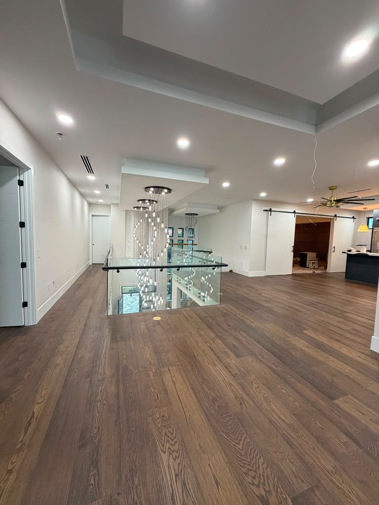 Open upper hallway with dark wood flooring, glass balustrade and modern chandelier