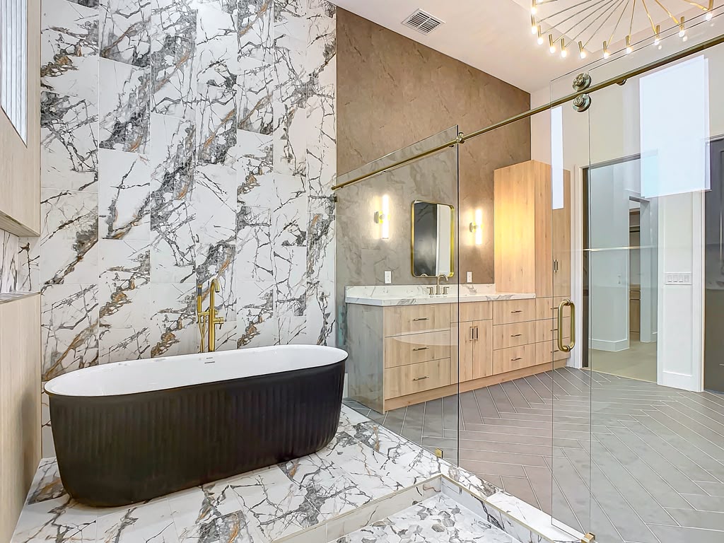 Primary bathroom with black fluted freestanding tub, white marble slab walls and gold fixtures