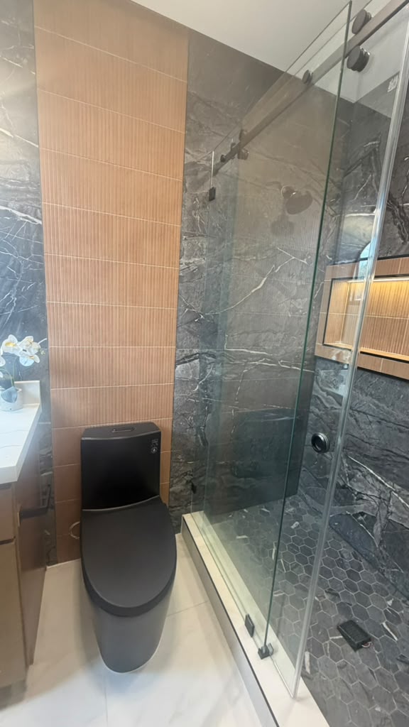 Bathroom with black wall-hung toilet, fluted wood accent tile and dark marble sliding-door shower